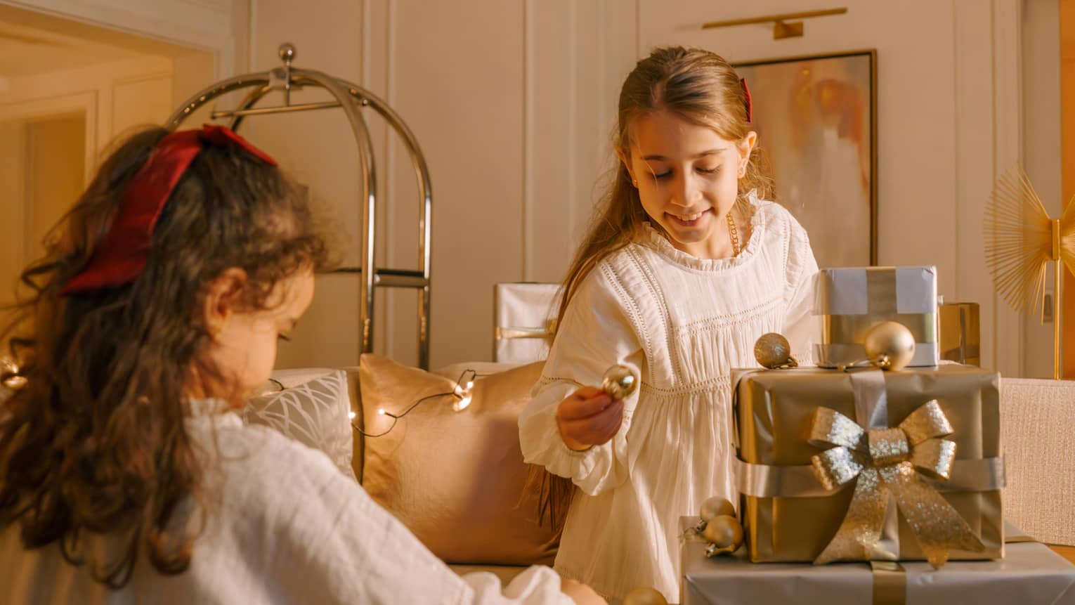 Two young children wearing white nightgowns look at a pile of presents wrapped in silver and gold paper and bows
