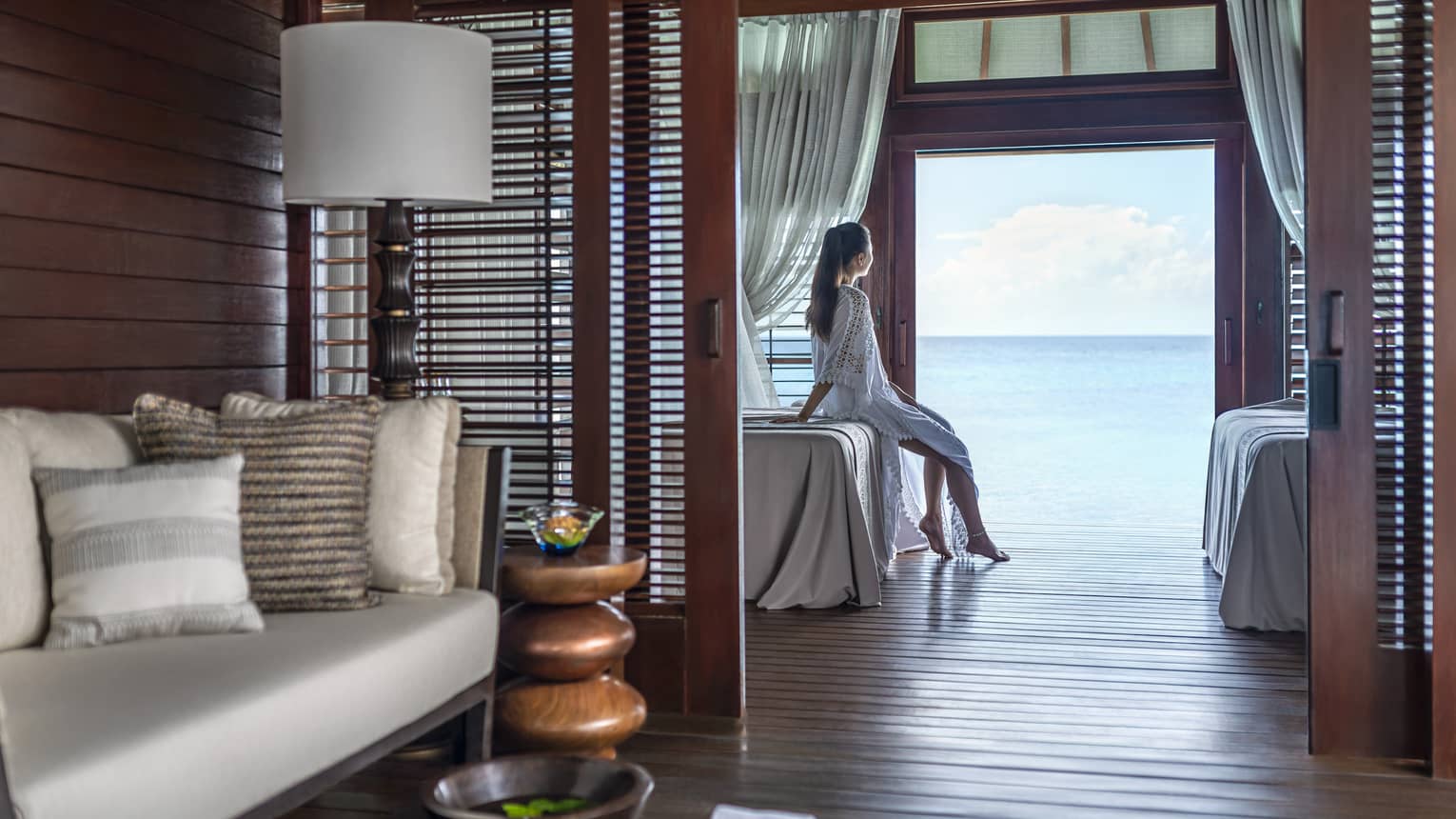 Person sitting on a massage bed in a serene spa treatment room with ocean view, surrounded by cozy seating and wooden décor