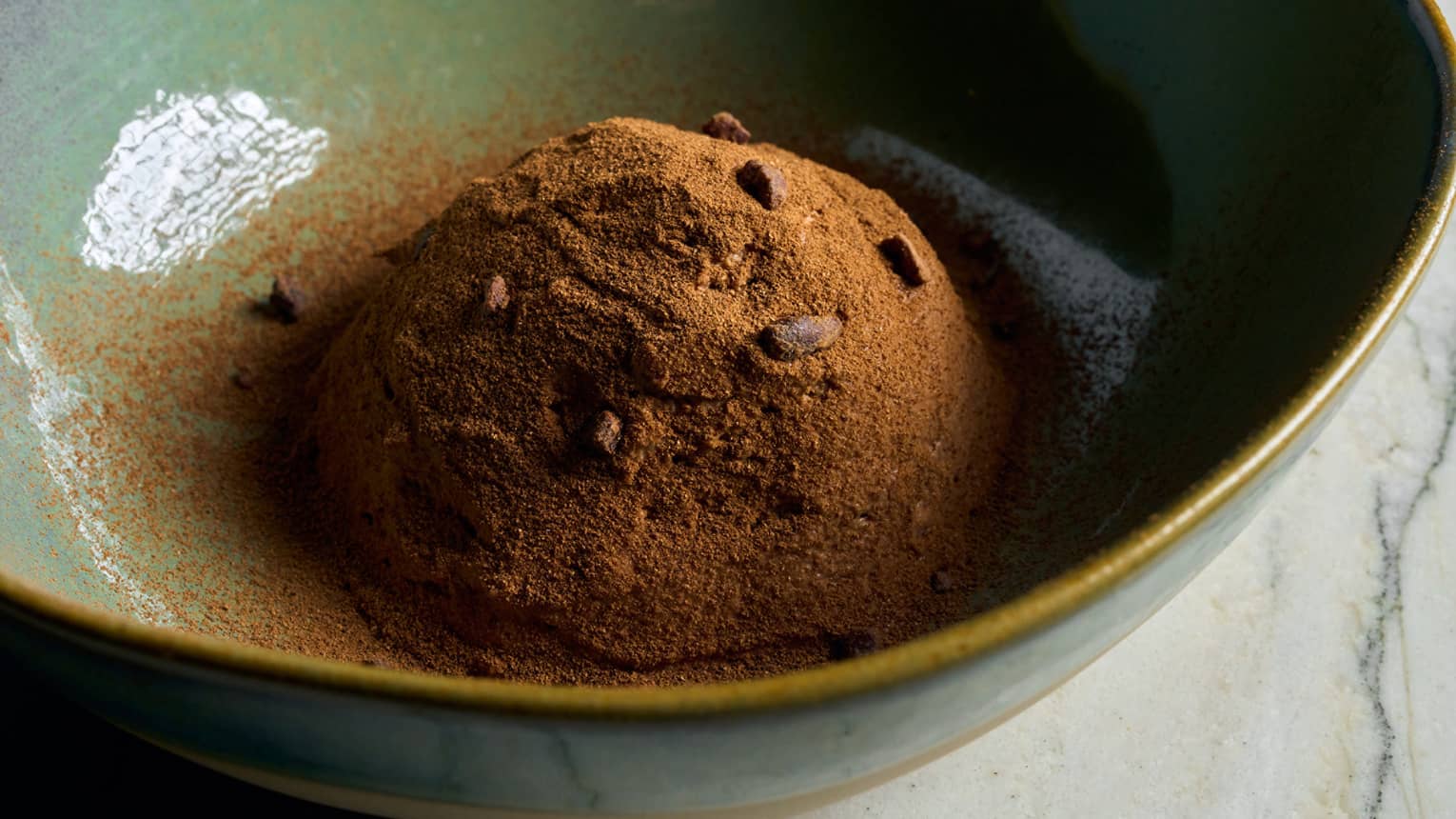 A green bowl with a cacao dessert topped with chocolate chips