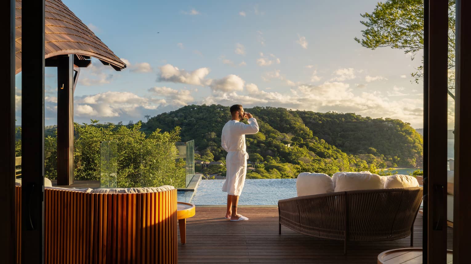 Guest wearing a white robe stand on a private pool deck overlooking a green seaside cliff