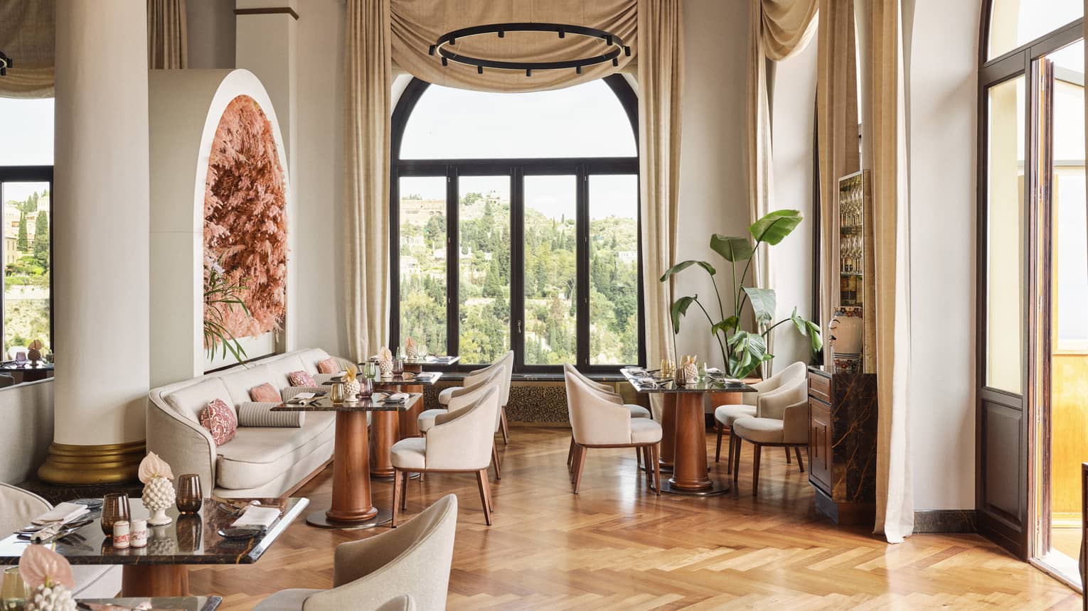 Restaurant dining room with parquet wood flooring, tall ceilings, white columns, banquet seating and large windows letting in natural light