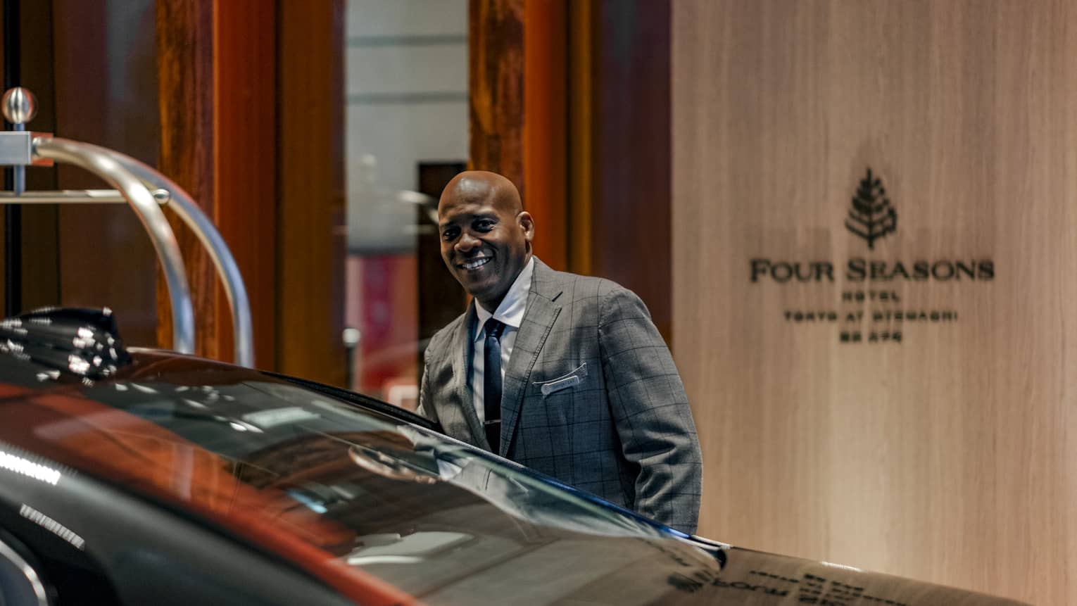 A man smiles as he gets into a black car outside a Four Seasons hotel