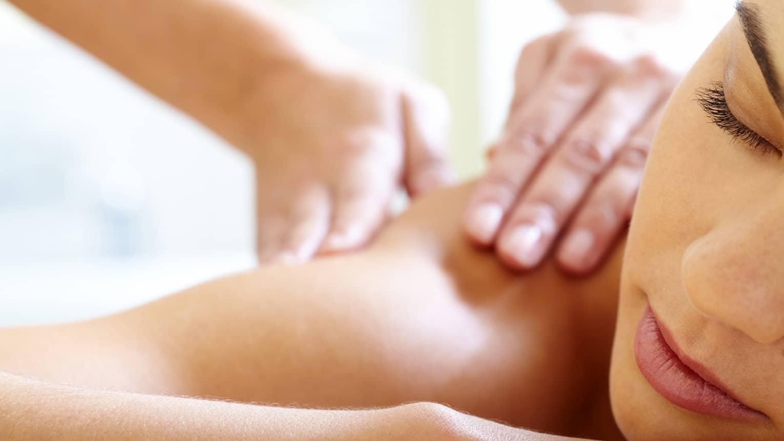 Close-up of woman's face with eyes closed, bare shoulder as she gets a Balinese massage
