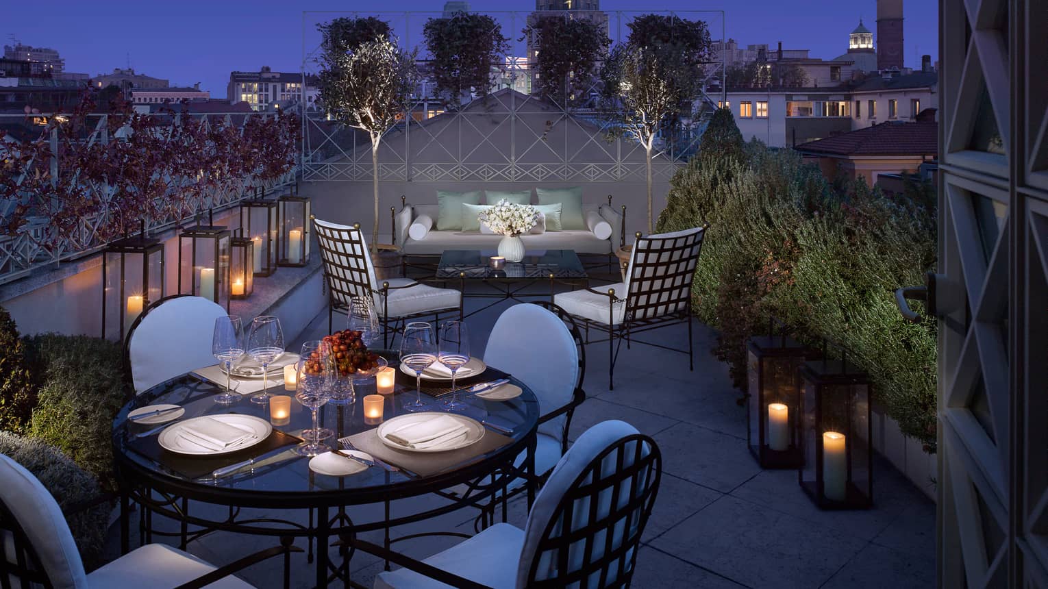 Penthouse Suite lantern-lined rooftop balcony, candle-lit dining table, patio sofa and chairs at night