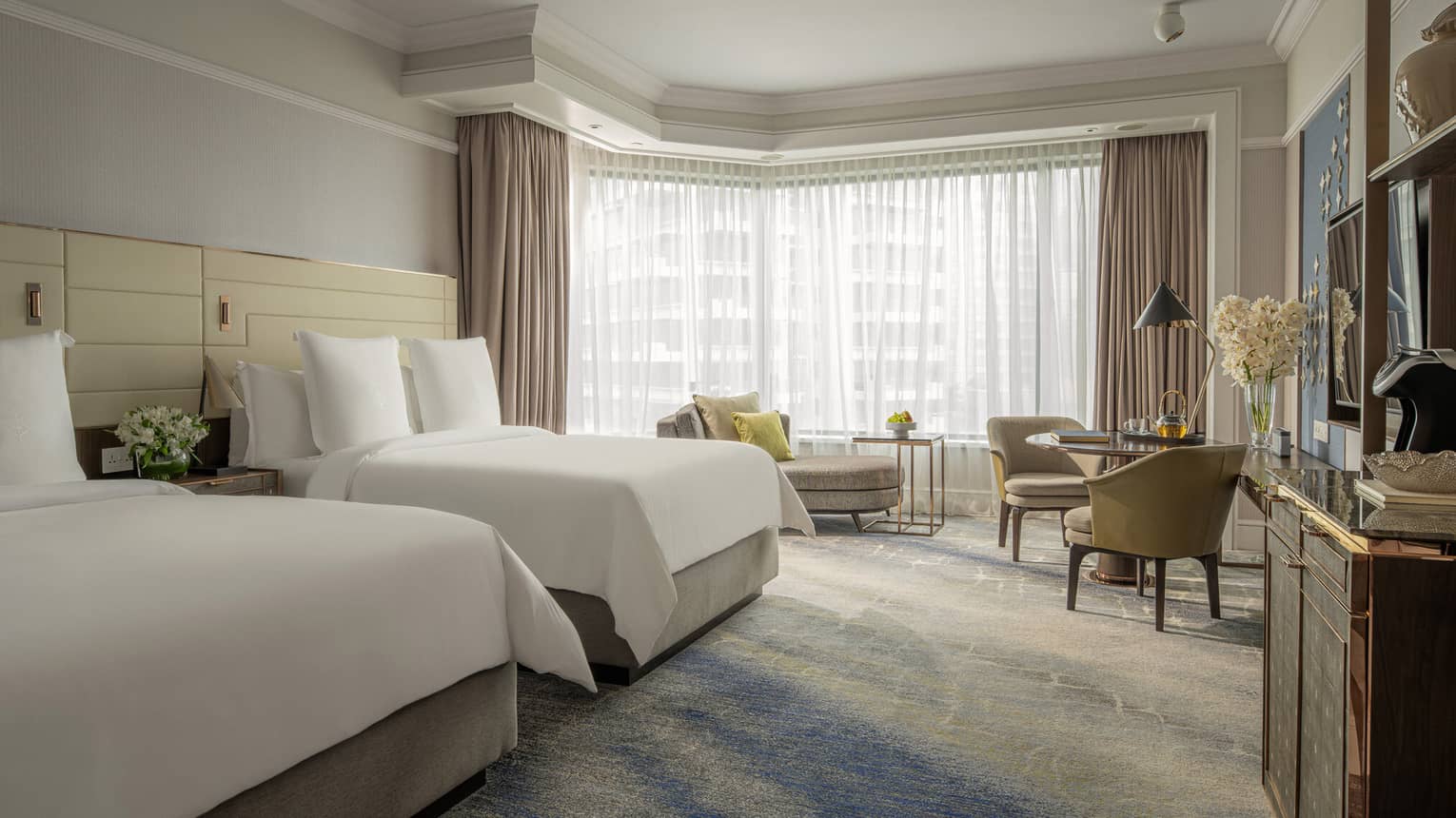 Guest room featuring two queen beds, a seating area and large windows with natural light.