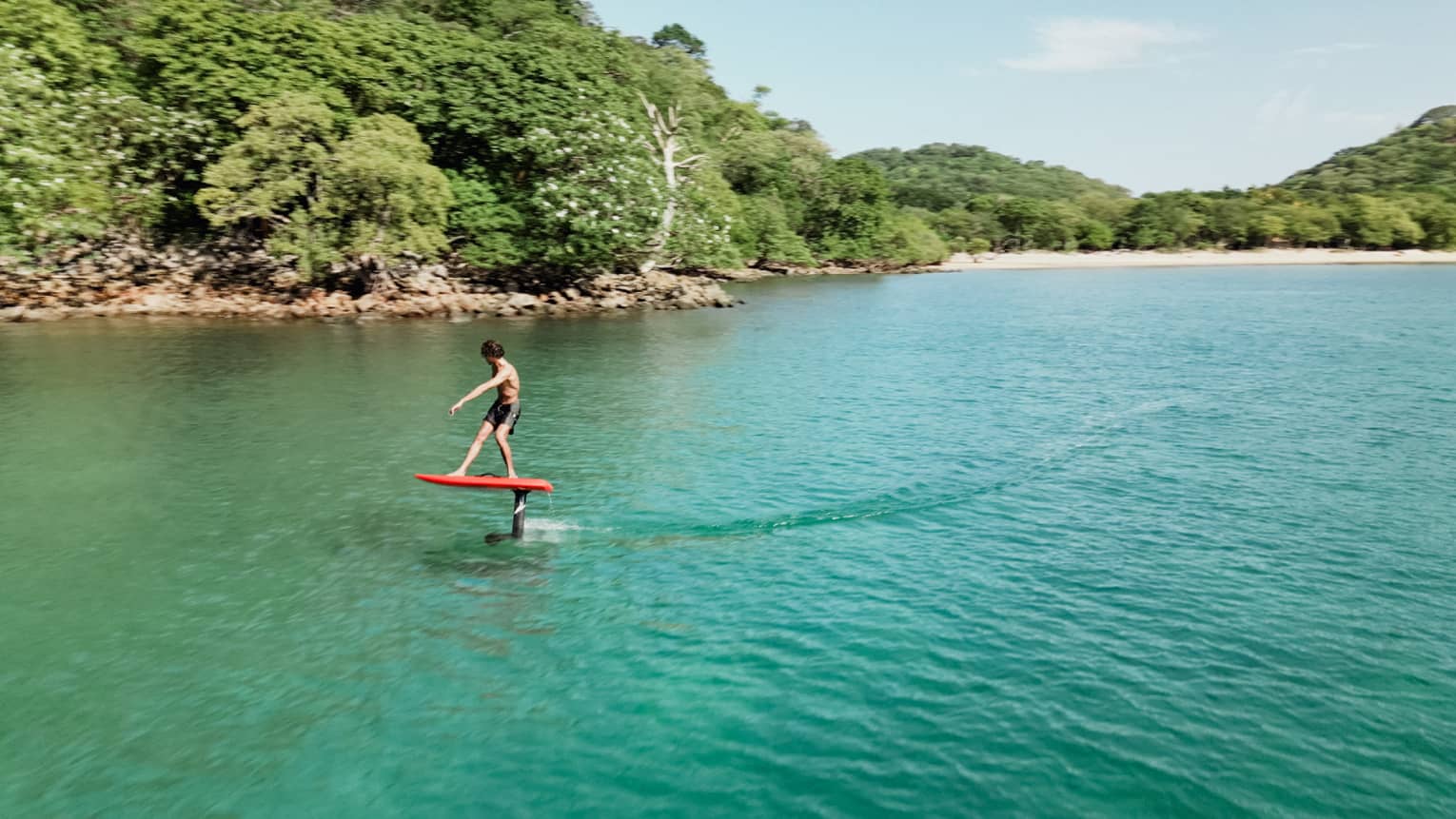 A surfer hovers over the water while riding a red e-foil surfboard