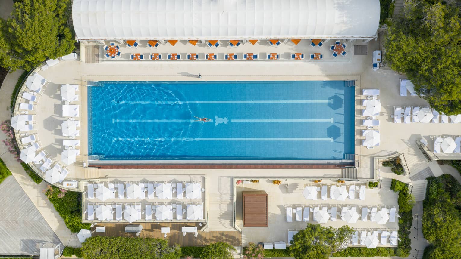 Aerial view of a luxury hotel, outdoor lap pool with surrounding white umbrellas and chairs