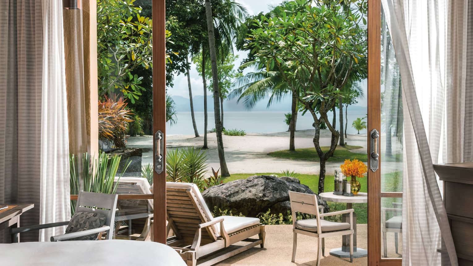 Curtains by open doors to ground floor pavillion, lounge chair by trees, beach views