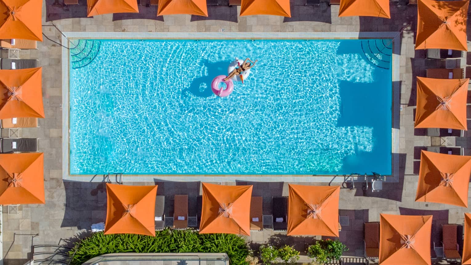 Aerial view of rectangular outdoor resort pool surrounded by orange umbrellas