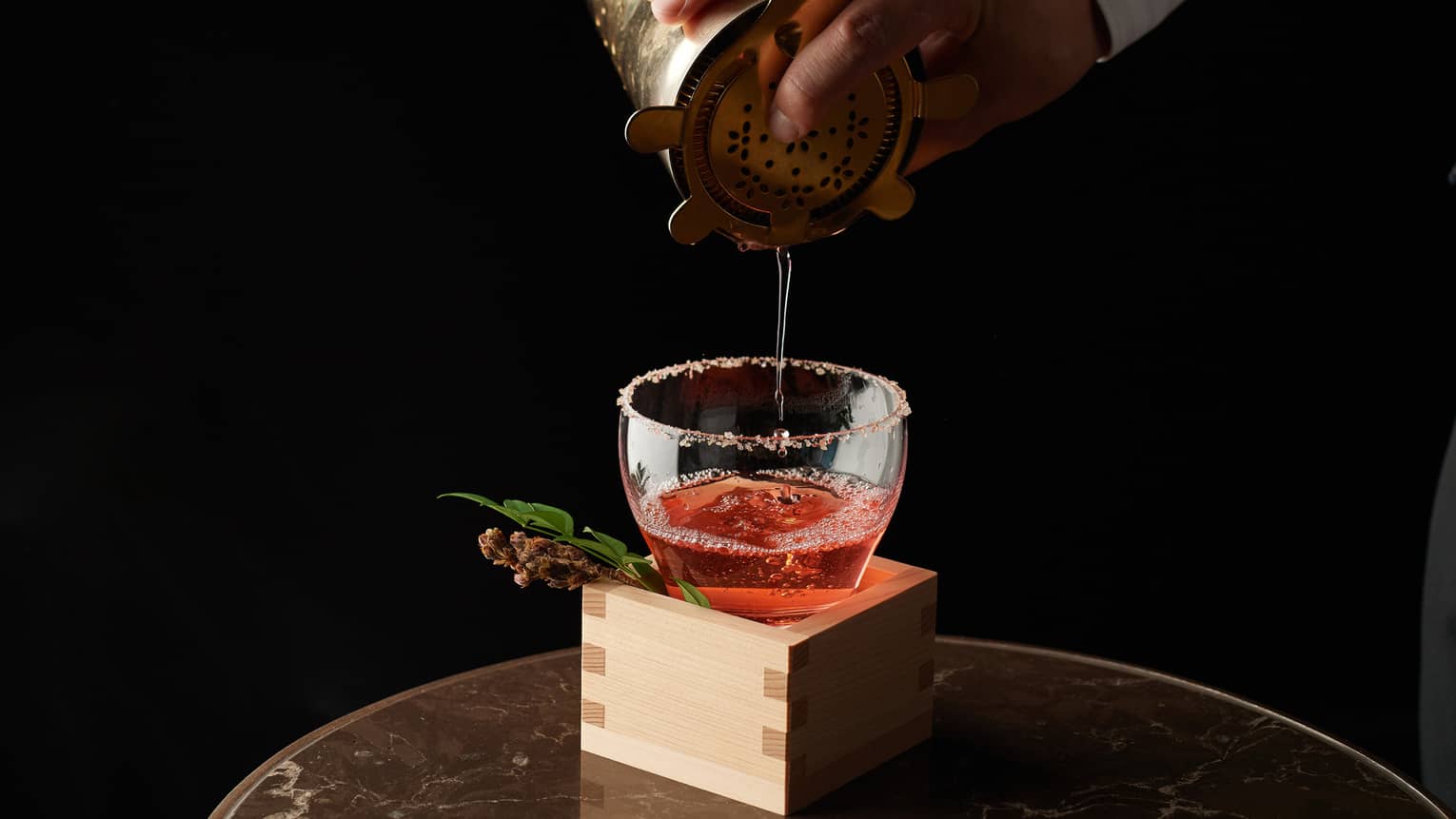 A cocktail that is light red in color on a wooden box.