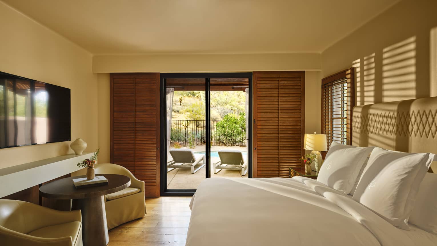 Bedroom with king bed, two arm chairs and small table, TV and walk-out terrace
