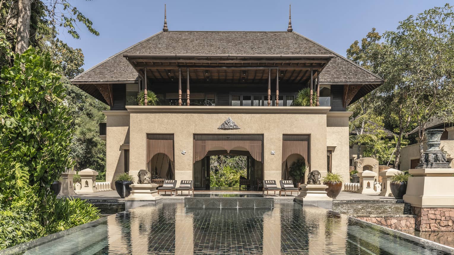 A large brown villa with a pool extending out from it.