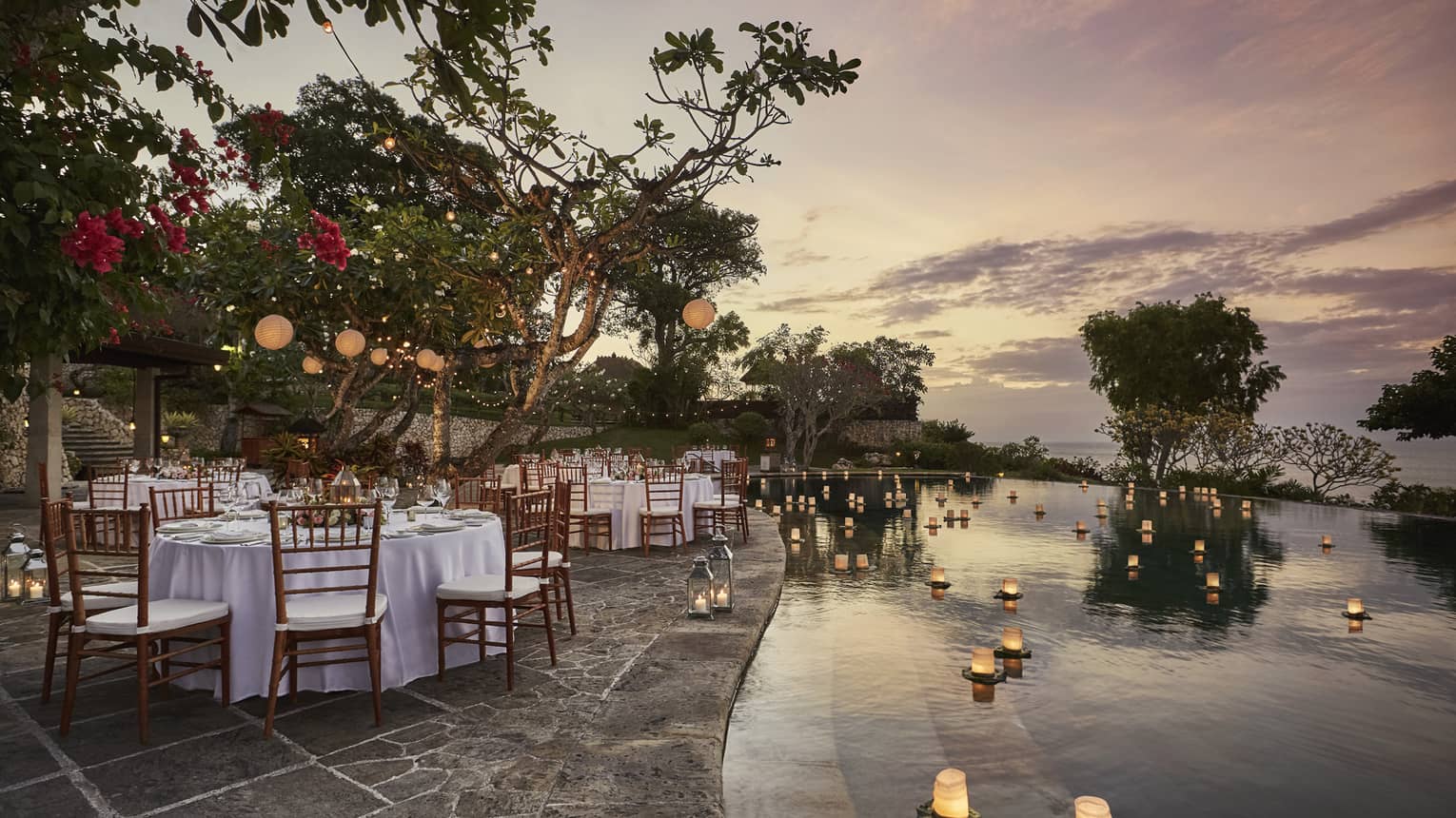 Pool Terrace banquet dining tables by candles floating on water at sunset