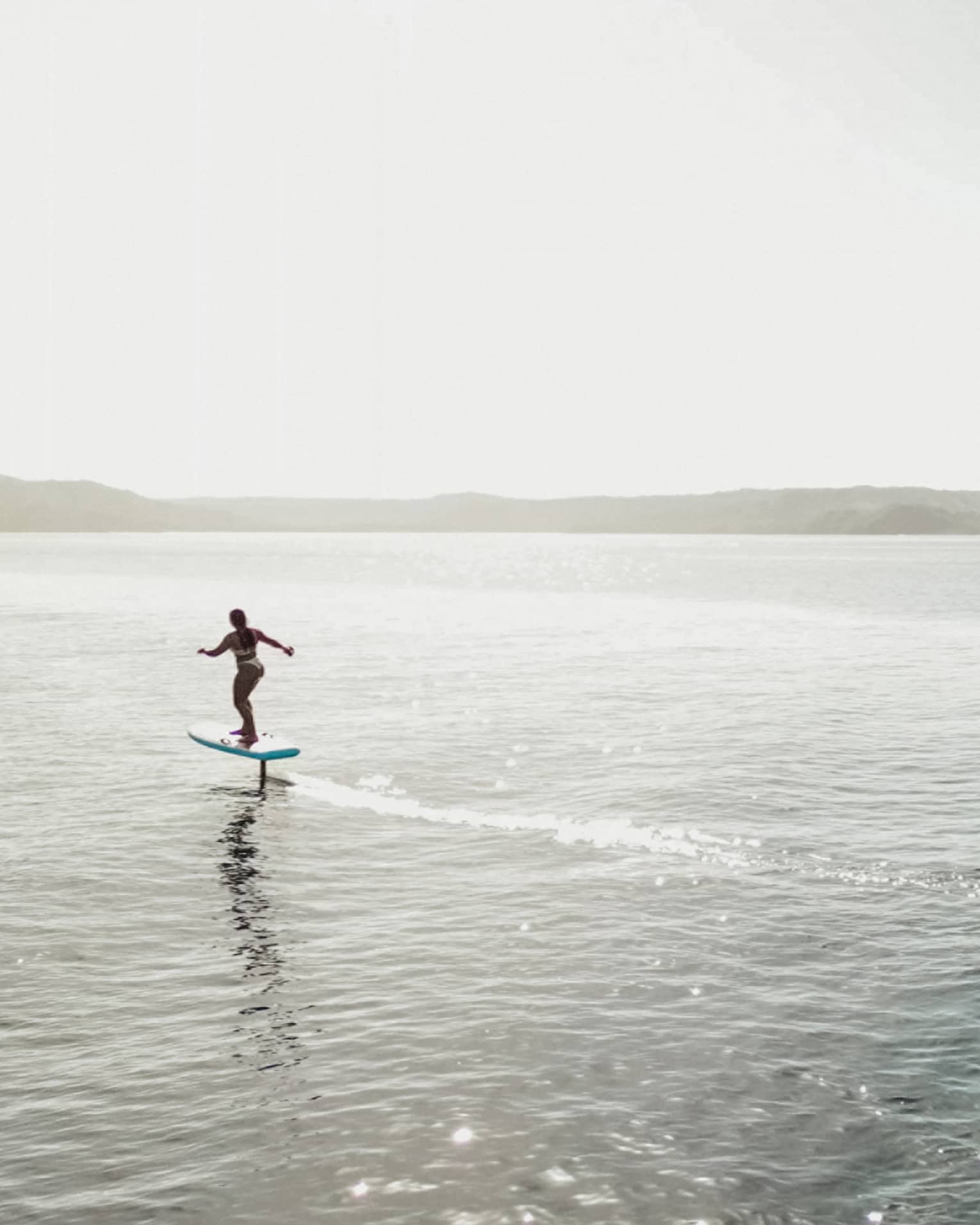 Two silhouetted figues riding e-foil surfboards in the water