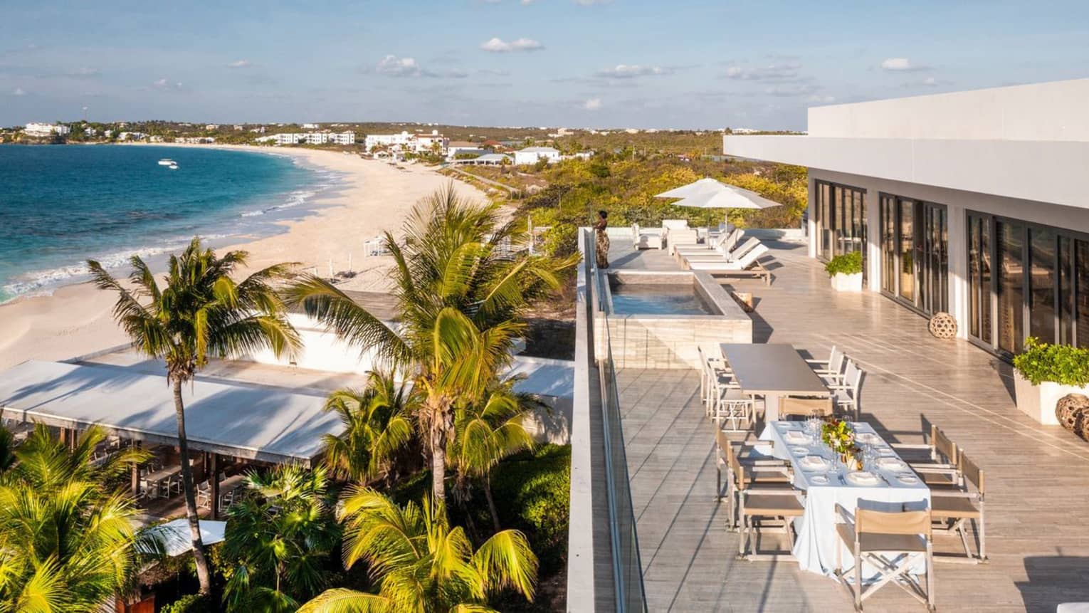 Rooftop terrace with a dining table, lounge chairs, pool and views of a tropical beach with turquoise water and palm trees