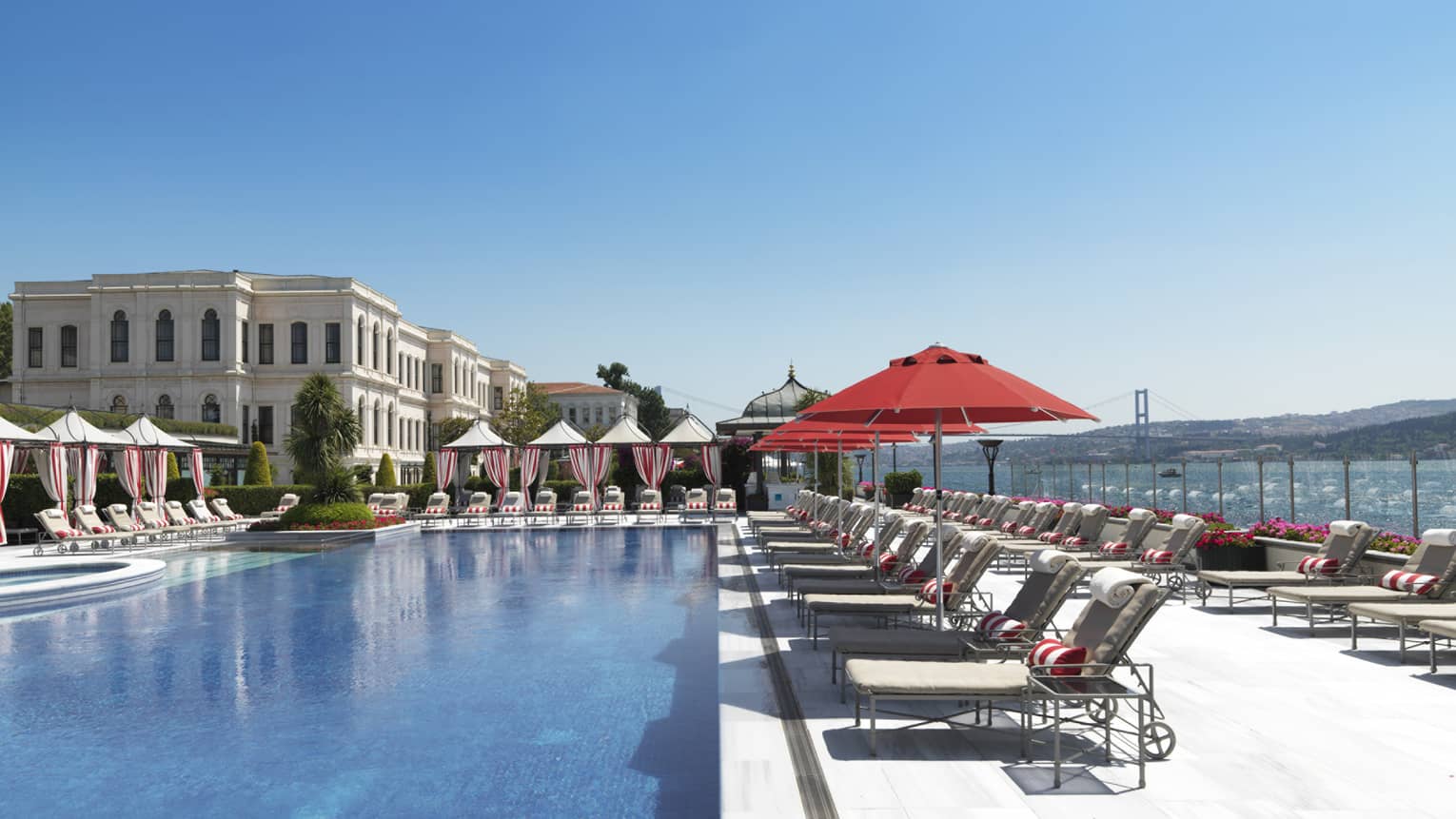 Patio lounge chairs and cabanas around outdoor swimming pool, hotel exterior