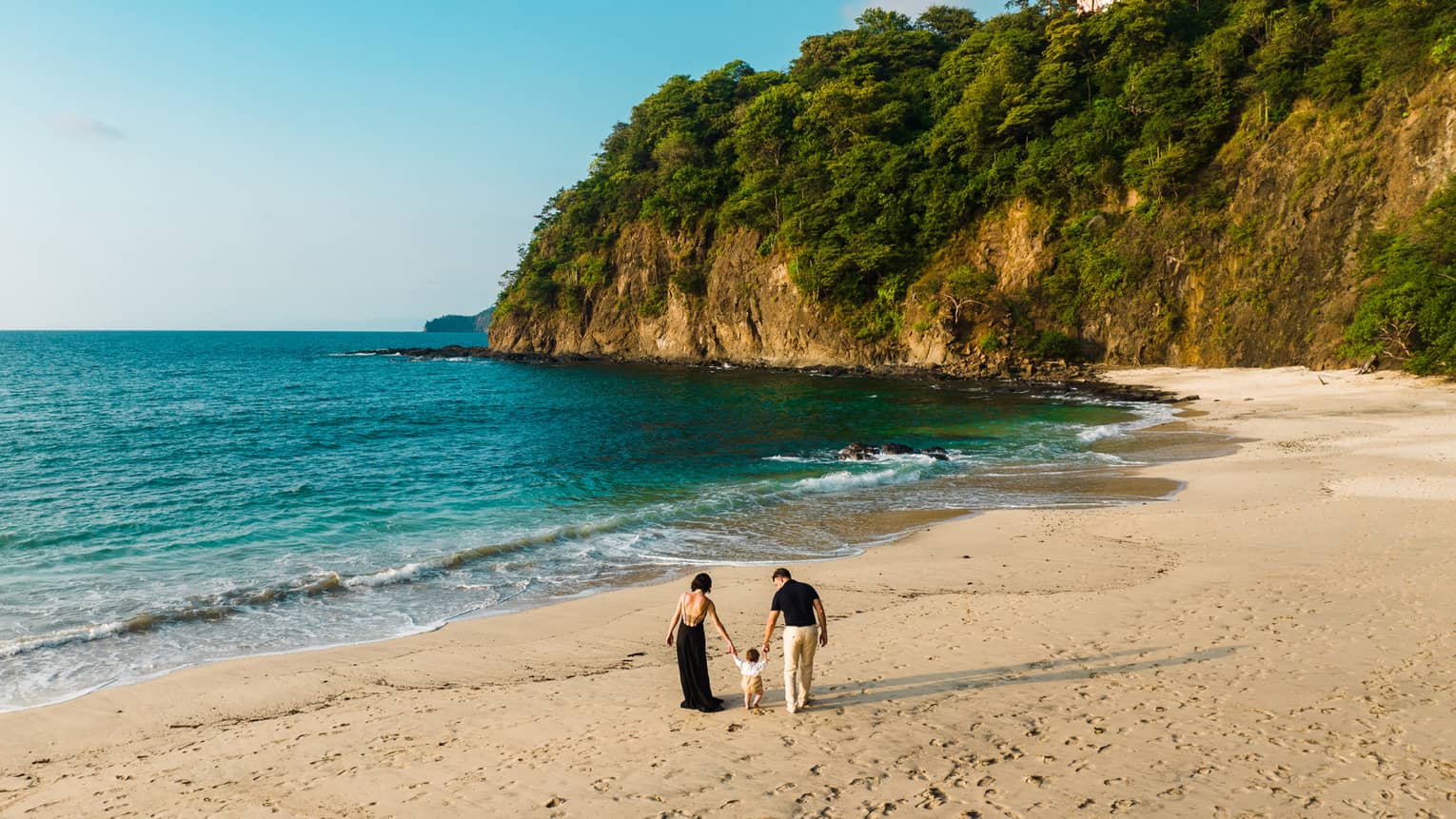 Two adults walk hand-in-hand with a small child along a beach