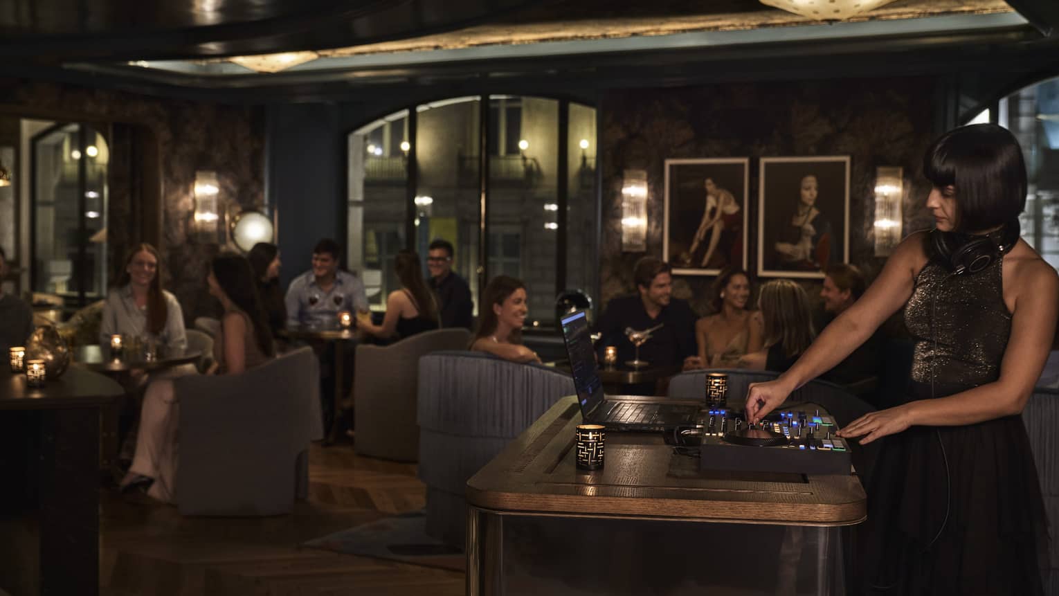 A female DJ performs in moody bar with dark chairs and walls
