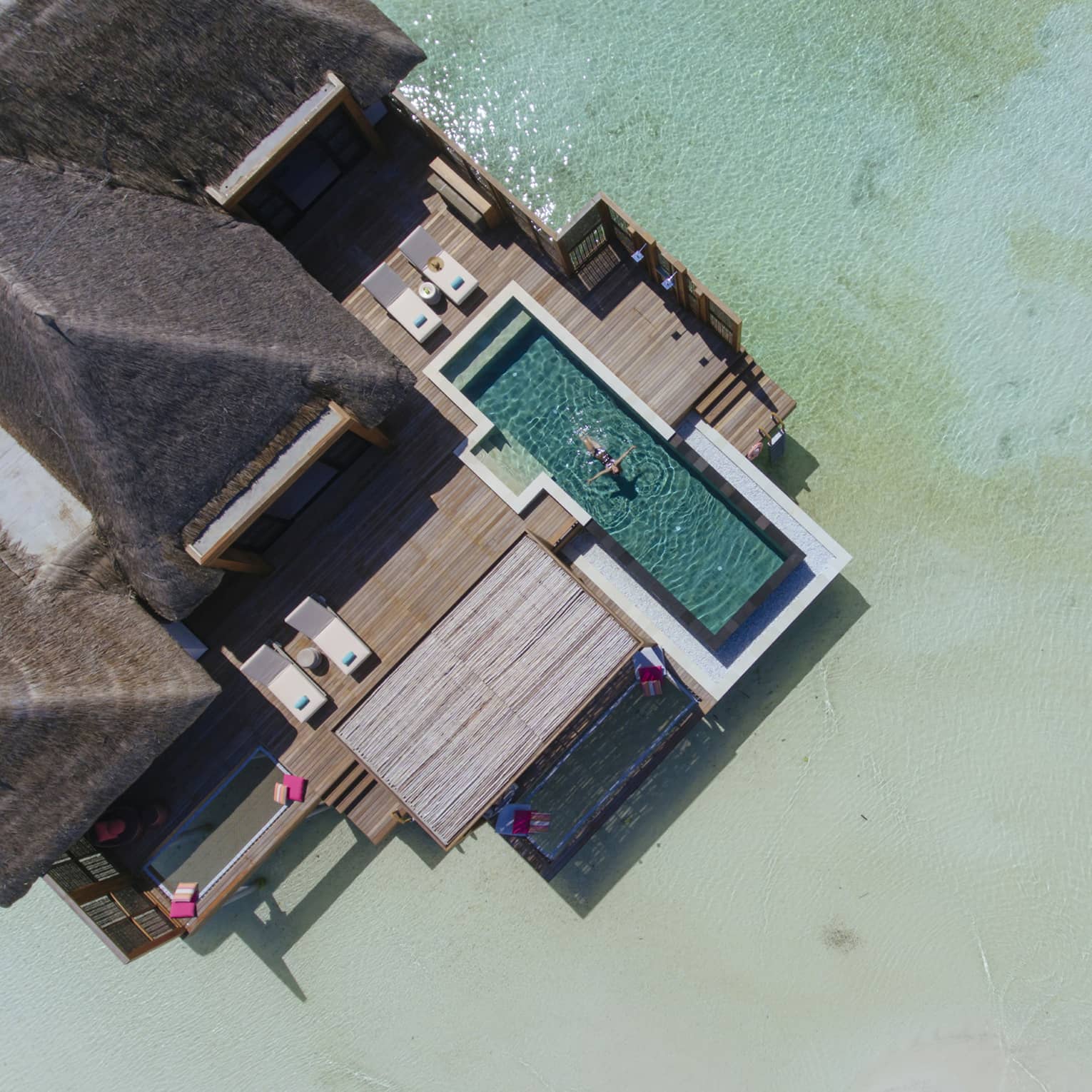 Aerial view of water suite, woman floats on back in private pool