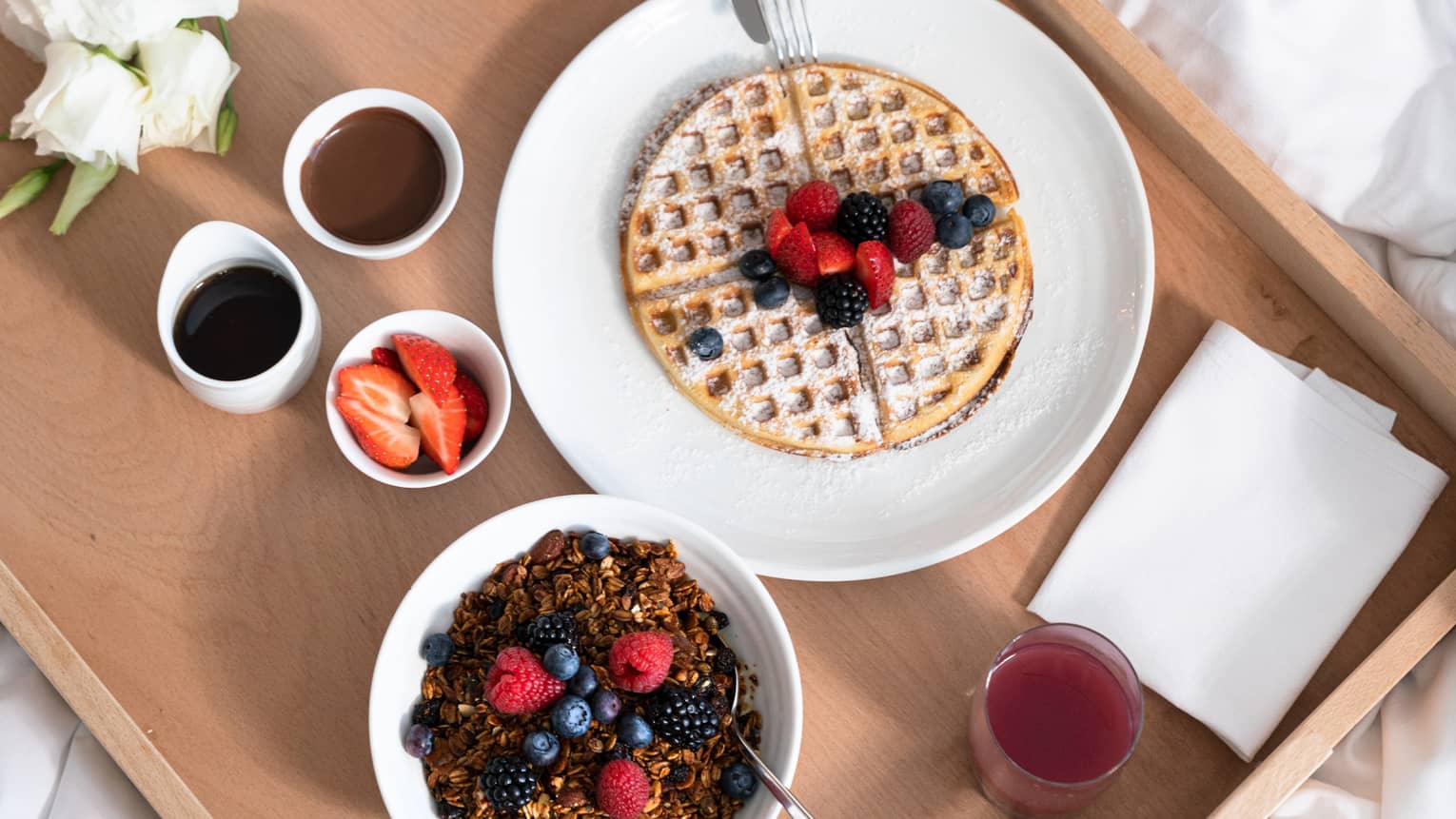 Waffles, fruit and coffee on a wooden tray on a bed