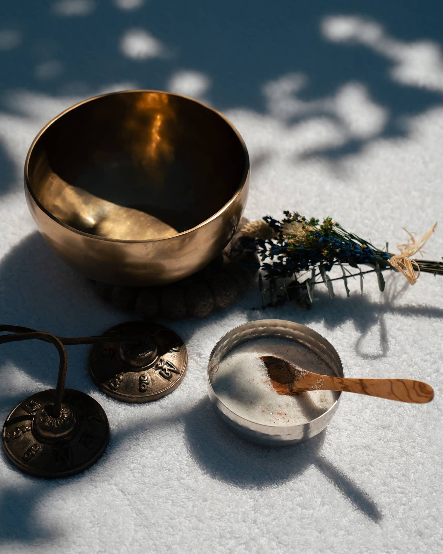 A small empty metal bowl, a small bundle of plants, a small bowl containing a whitish substance and a small spoon, and a set of small metal bells.