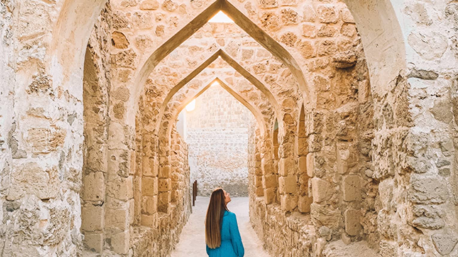 A woman stands underneath a stone pathway.