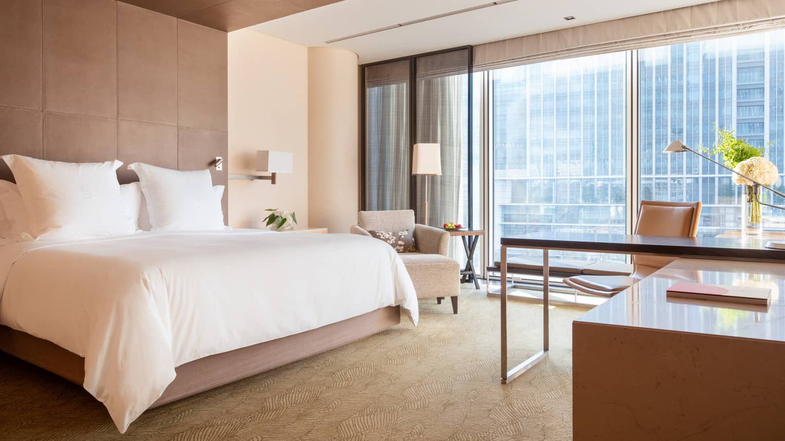Guest room with large windows, city views, king bed, lamp, armchair and workspace