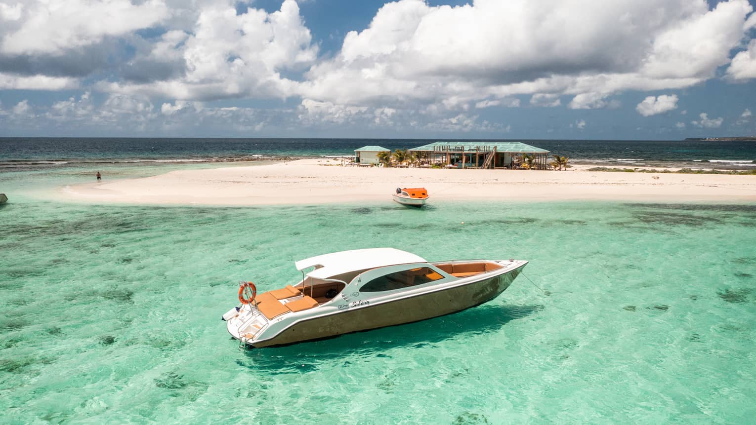 Luxury speedboat floating in clear turquoise water near a sandy island with a beach hut.