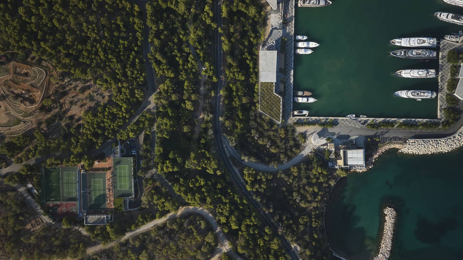 An aerial view of a forest, tennis court and boats.