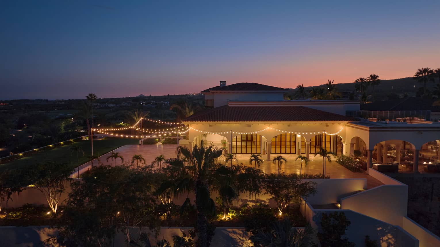 Bird's-eye view of an oudoor event space brightly lit for the evening, surrounded by palm trees and adjacent to a building