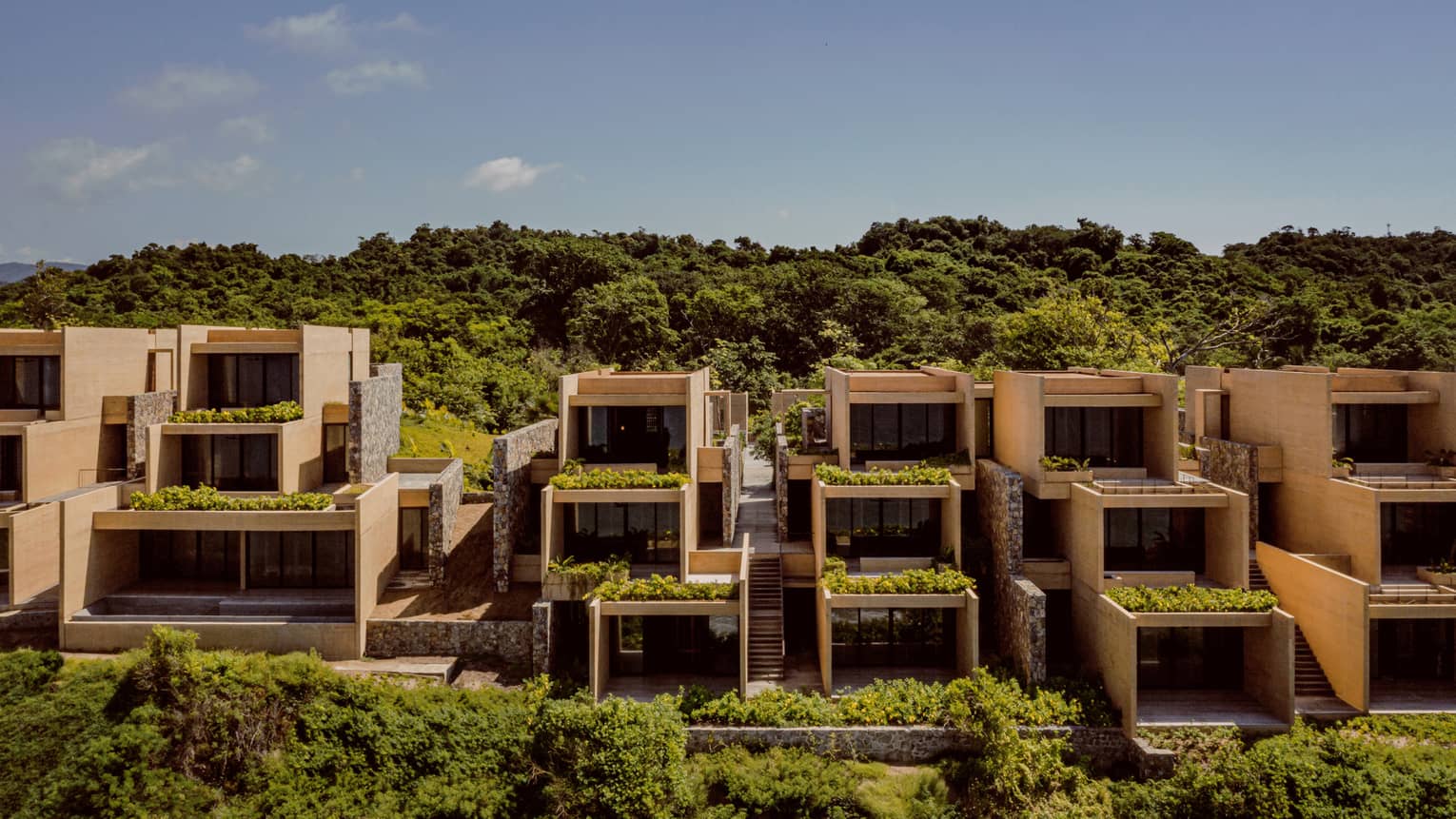 Exterior of a resort's three-level, stacked building, with trees in the foreground and background