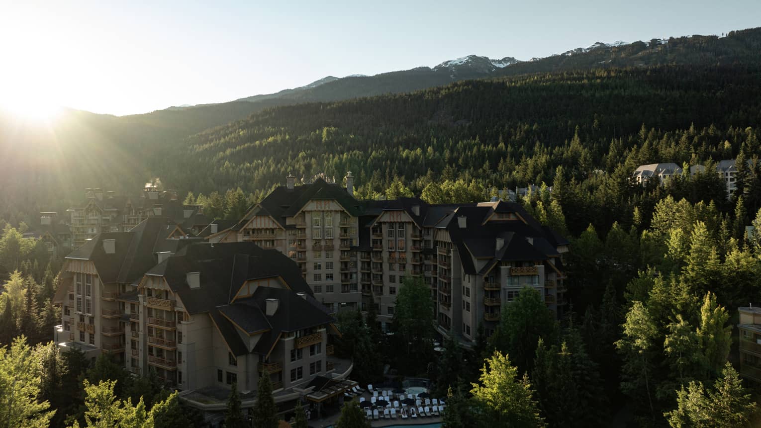 The sun shines on a mountain resort surrounded by a forest of green