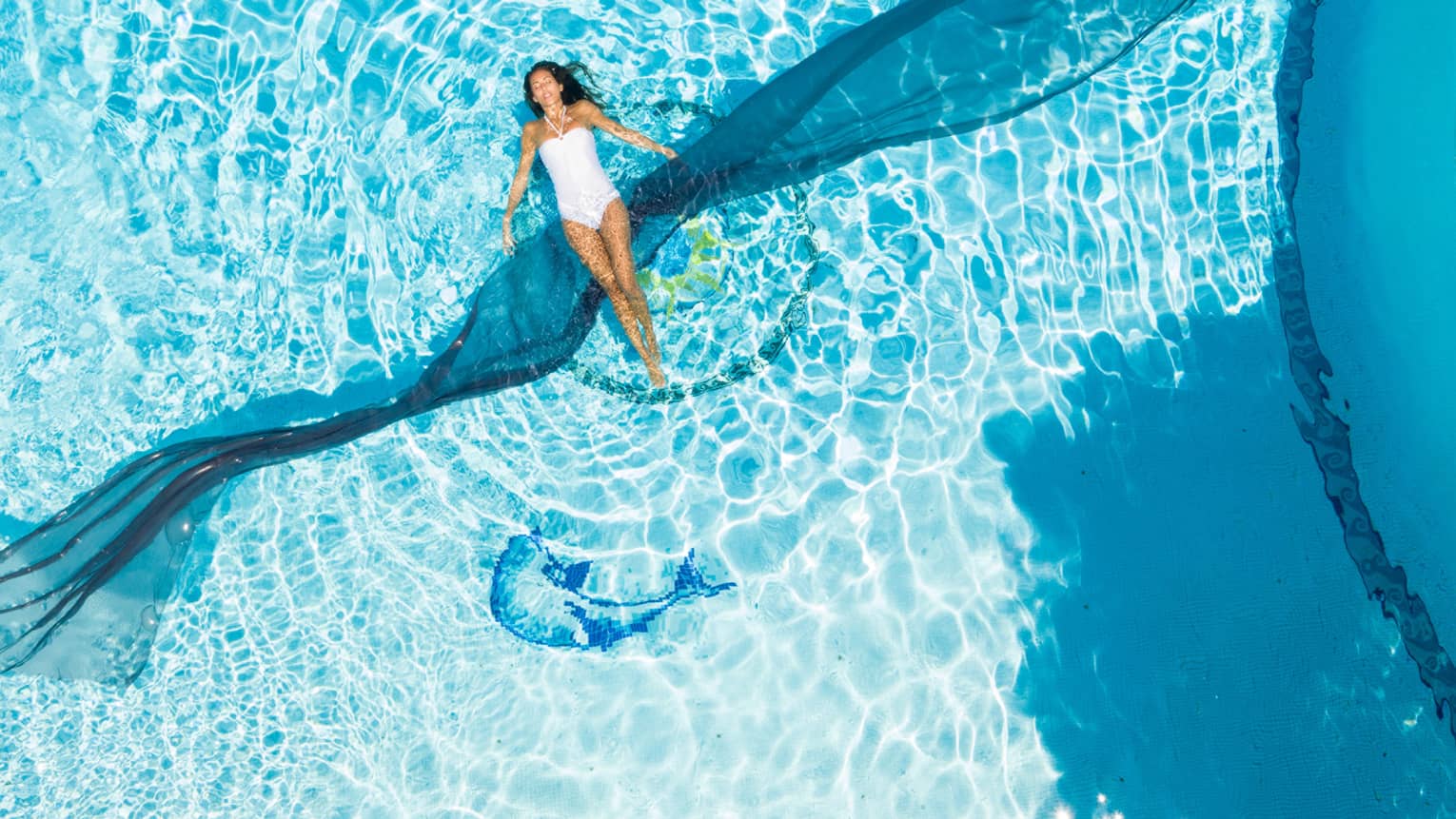 Woman in white swimsuit bloating in pool's sparkling water, blue dolphin image on bottom