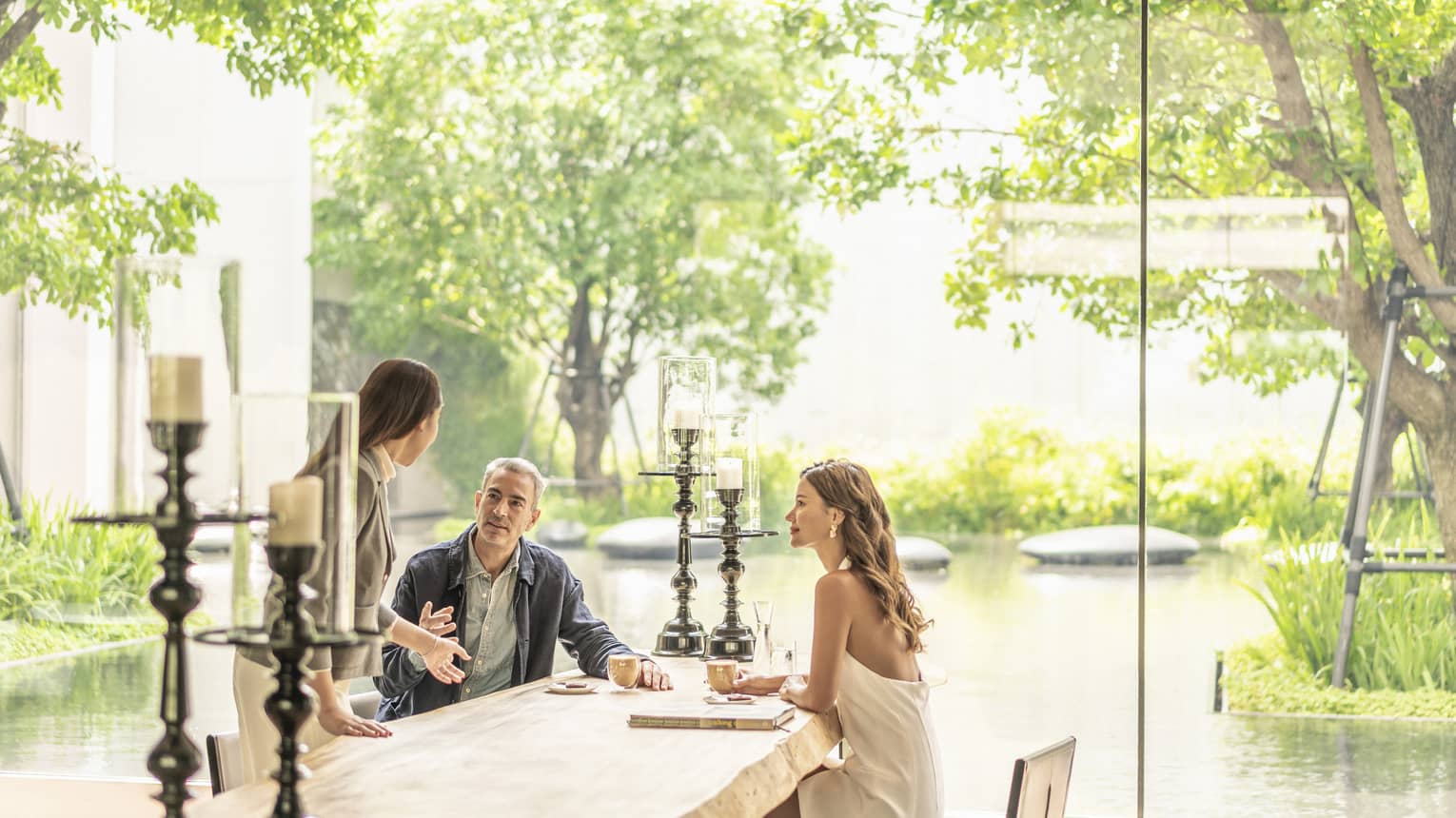 Couple chats with staff member at table at The Lounge, pond views