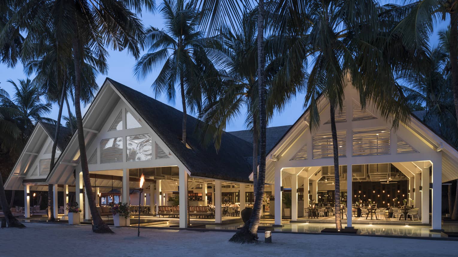 Exterior of a Maldives restaurant, large palm trees in front, three pavilions
