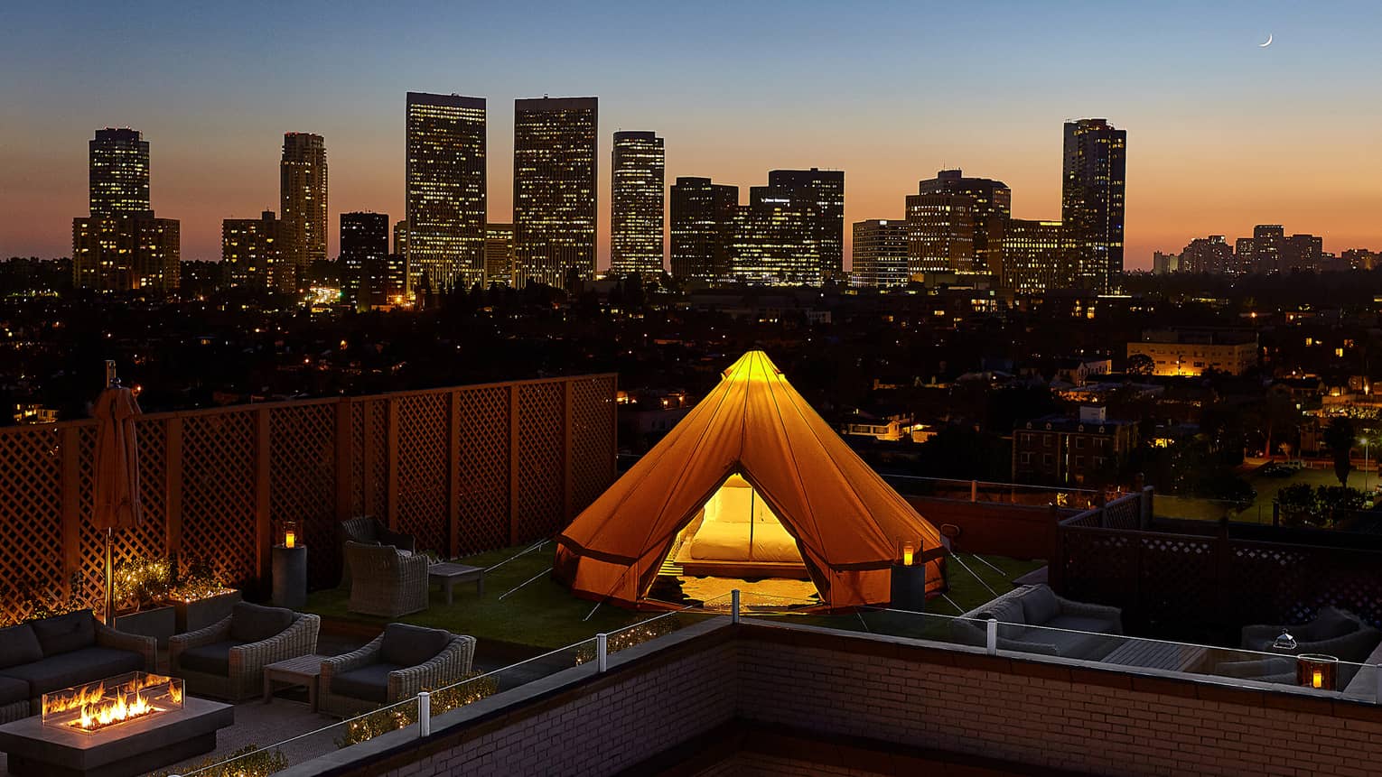 Glowing white tent, bed on rooftop patio by chairs, outdoor fireplace, Beverly Hills sunset city views