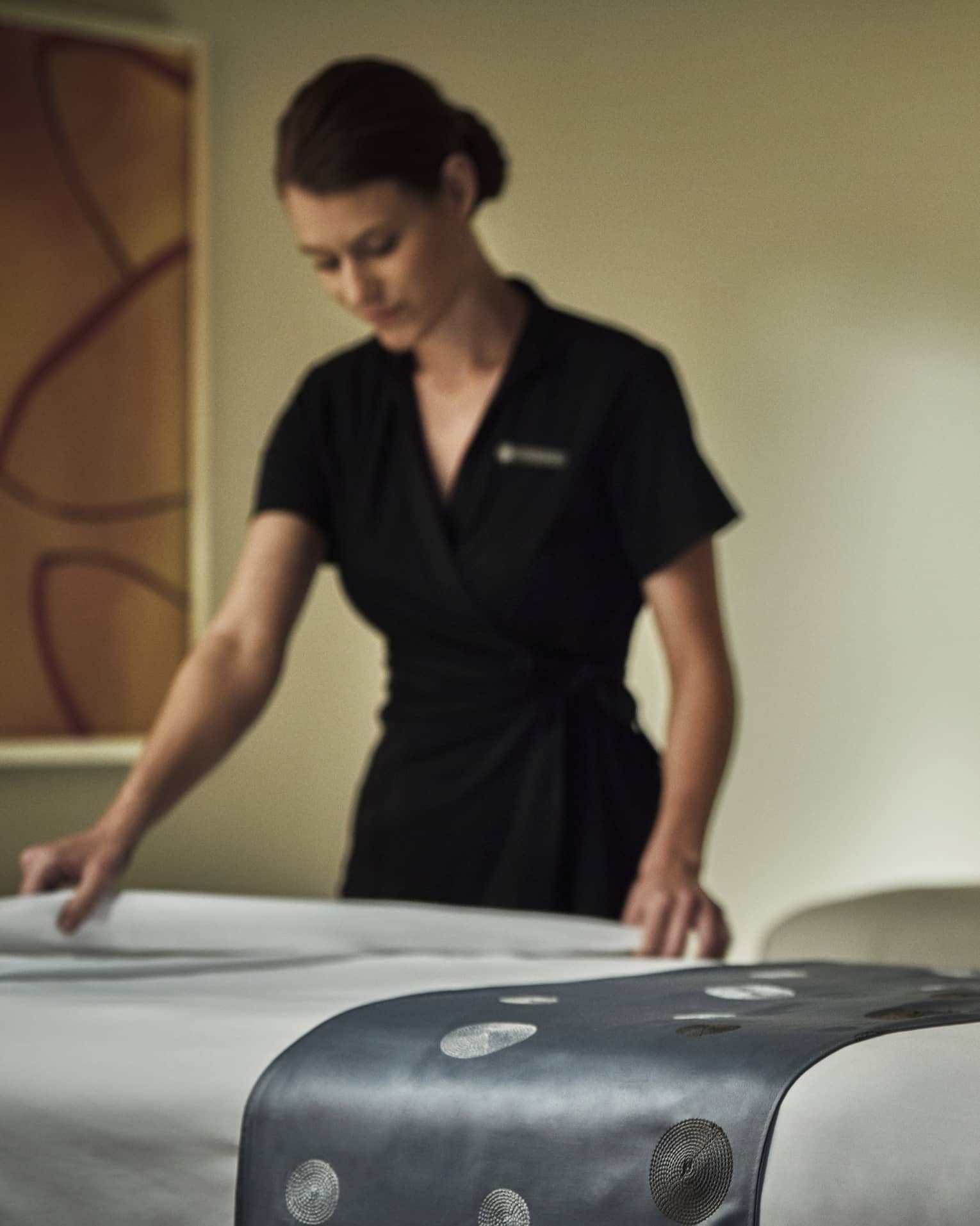 Spa attendant in black dress folds down white sheet on massage table