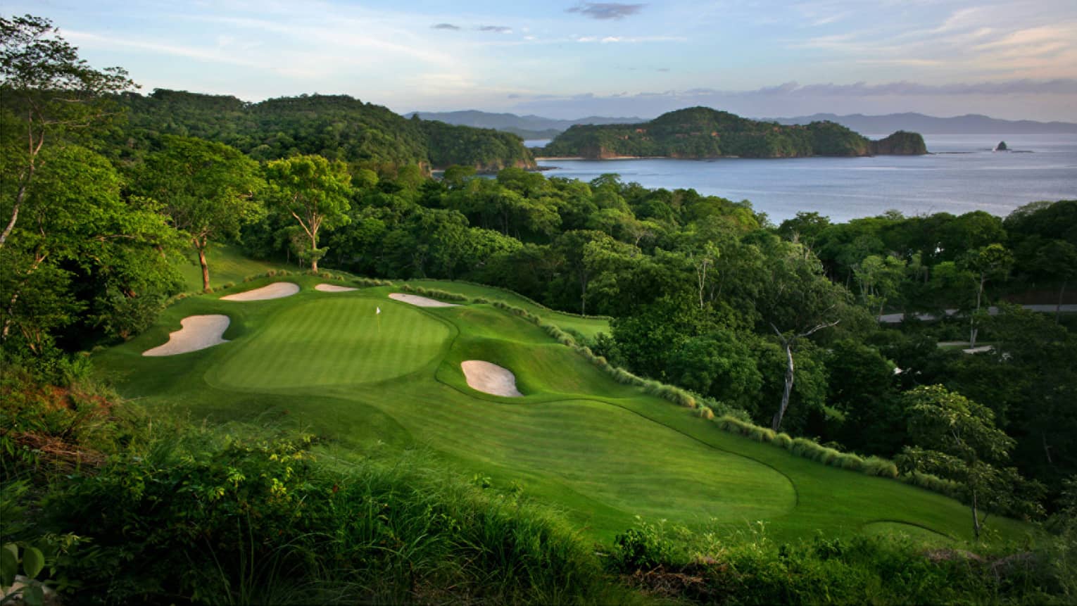 Aerial view of Hole 17 featuring a green in the foreground and the ocean and rock outcroppings in the background