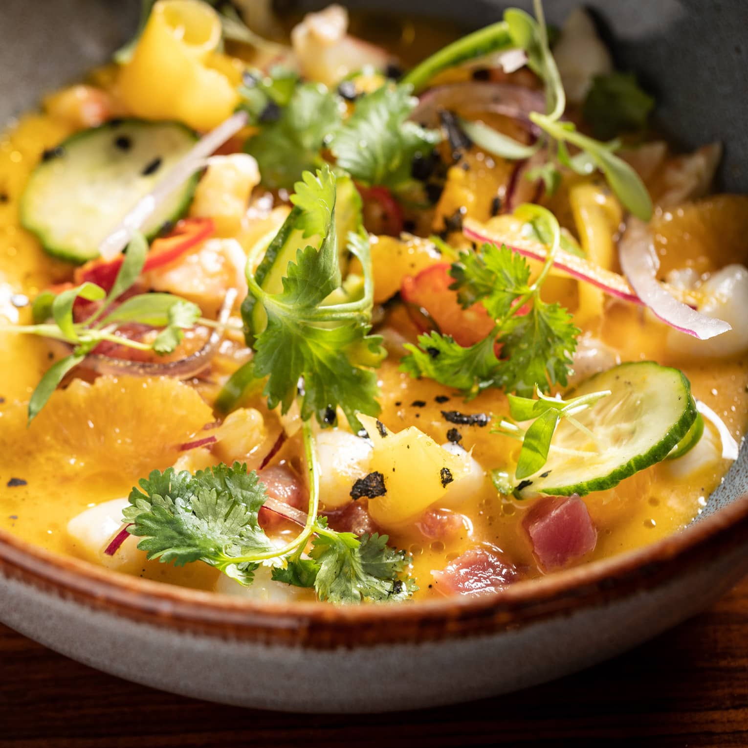 A bowl of yellow ceviche with scallops and shrimp garnished with citrus and cilantro.