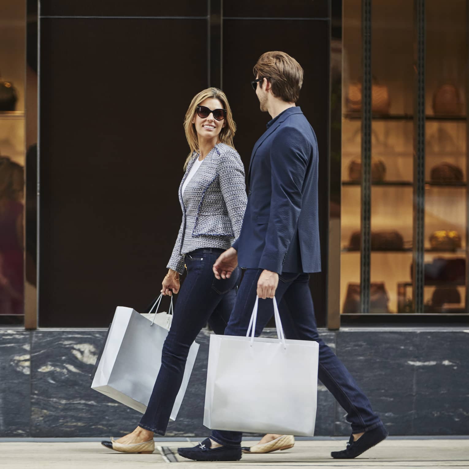 Man and woman walk down street, carry large paper shopping bags