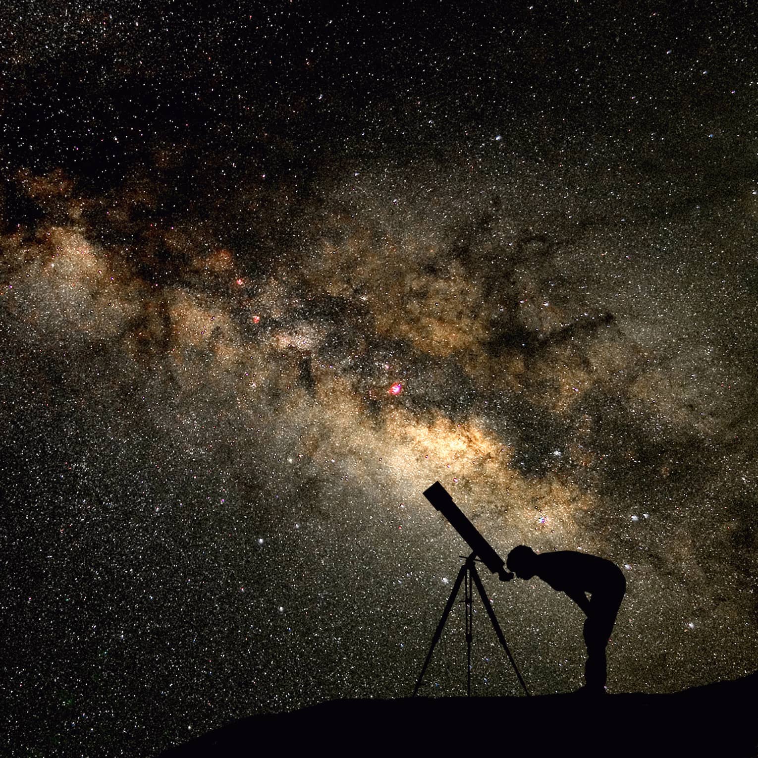 Silhouette of stargazer leaning into telescope against a starry sky, milky way