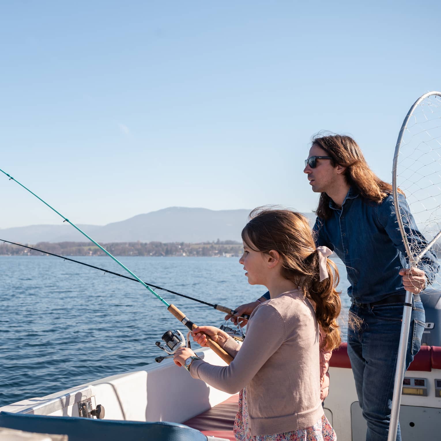 Man holding net and fishing rod, and girl standing in boat, holding fishing rod