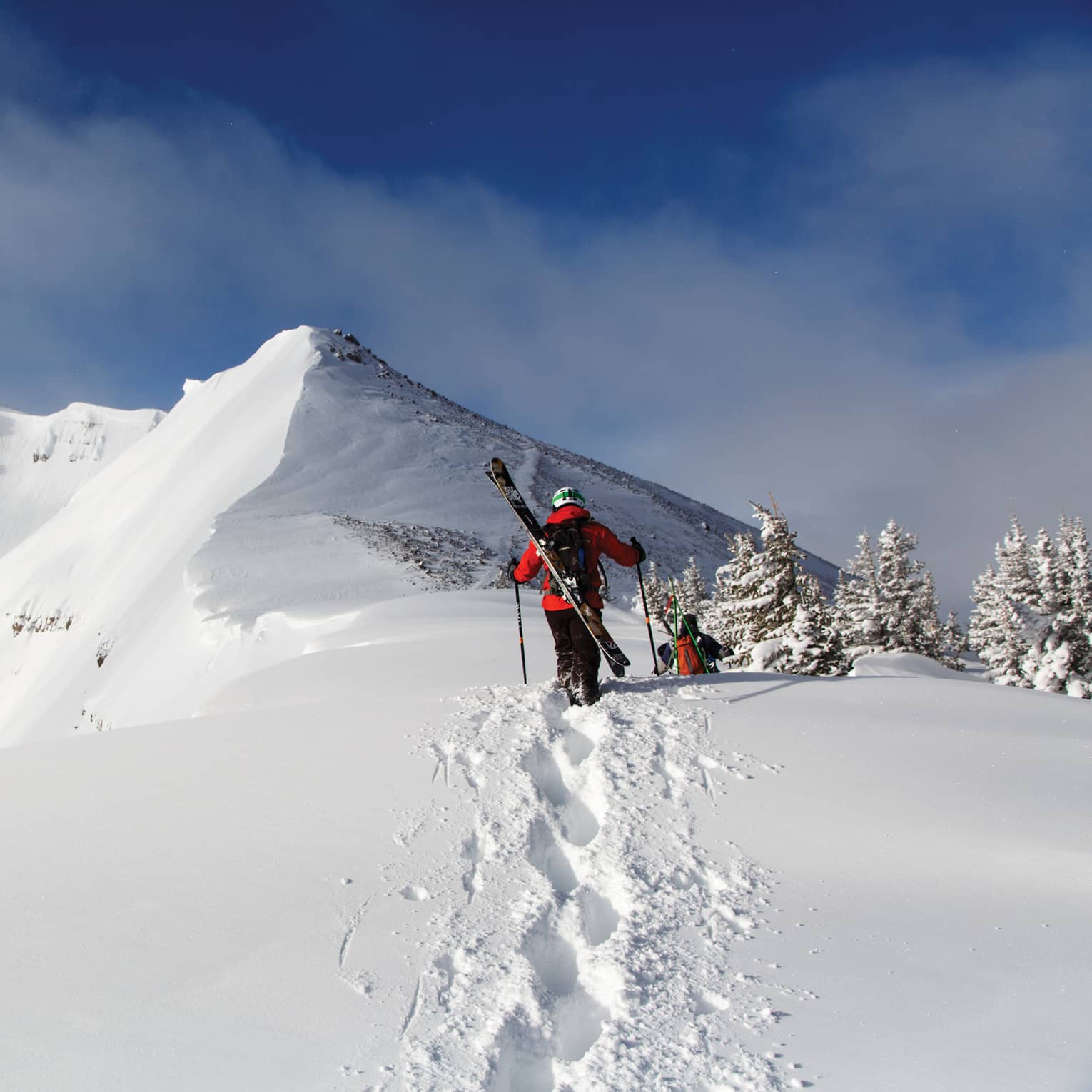 Two people with skis on their backs walking in snow.