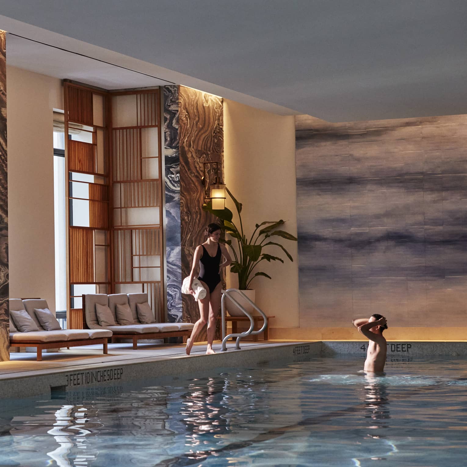 Woman standing on side of pool holding towel, man standing in pool.