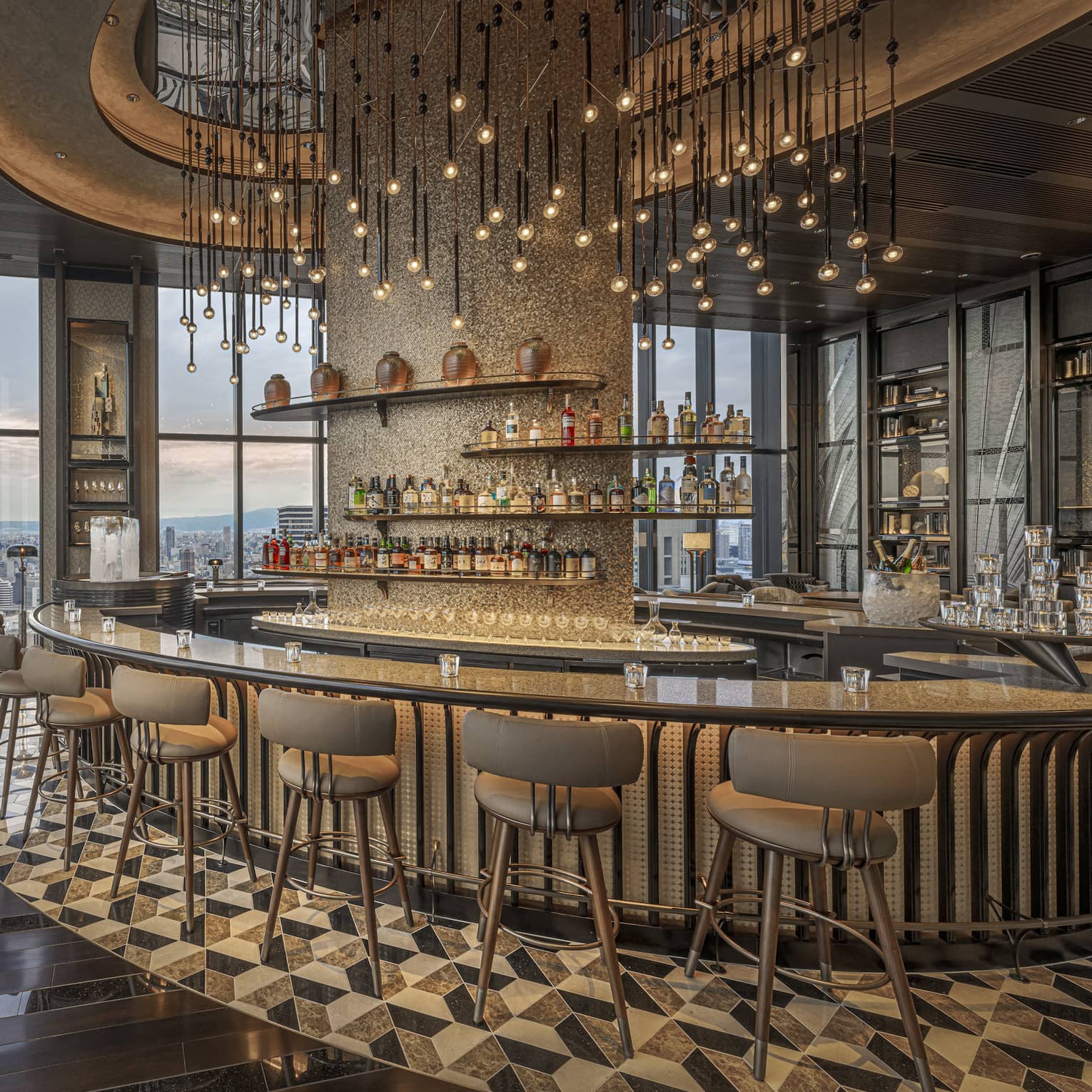 Large circular granite-topped bar in a modern luxury restaurant surrounded by a bank of windows overlooking city at dusk.