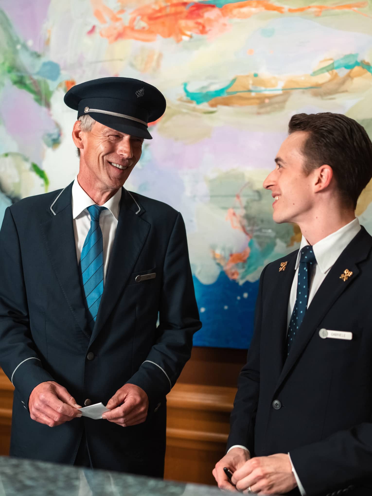Two people in suits stand behind hotel welcome reception counter