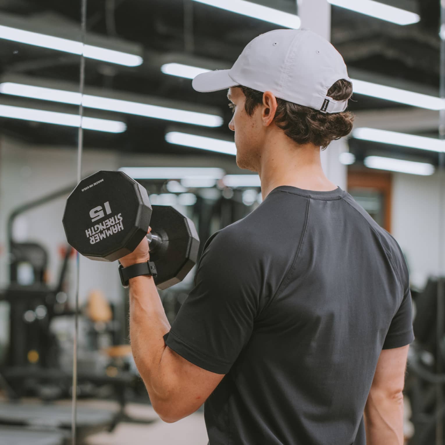 Person at a gym and standing in front of a mirror lifting weights.
