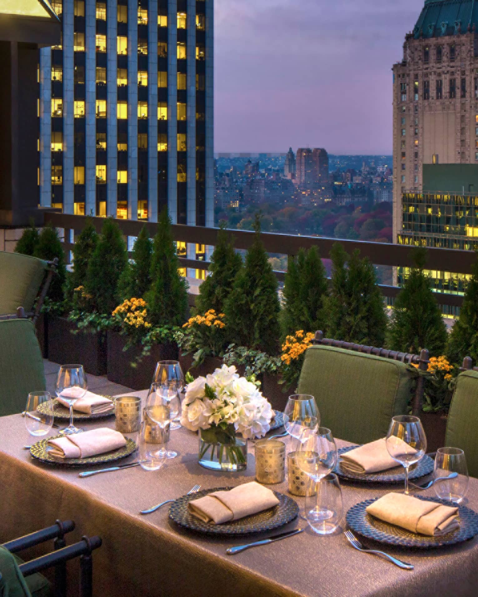 Private patio dining table with plush green cushions on chairs on rooftop terrace, city views at dusk