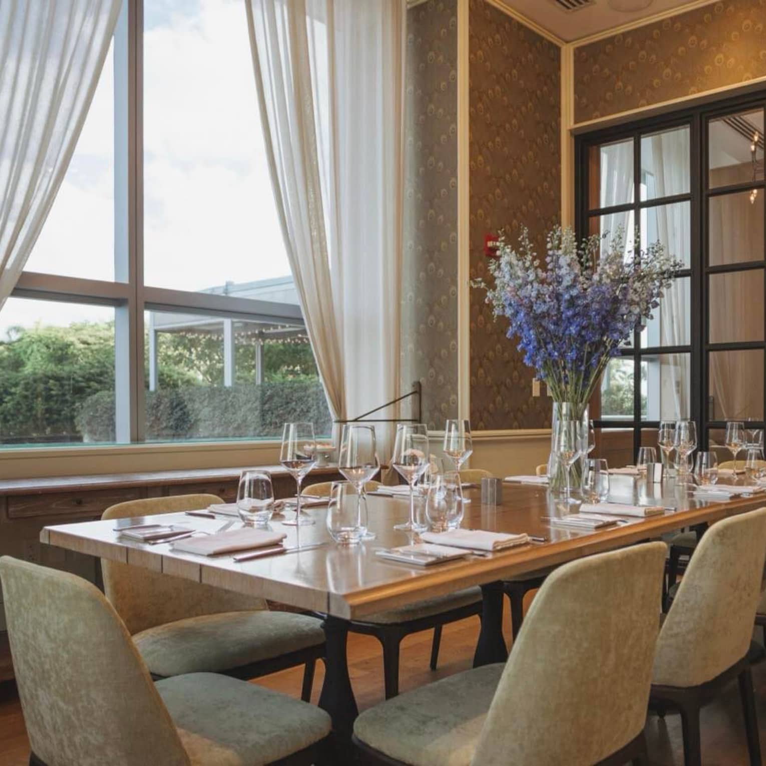 A large dining table with blue flowers near a large window.