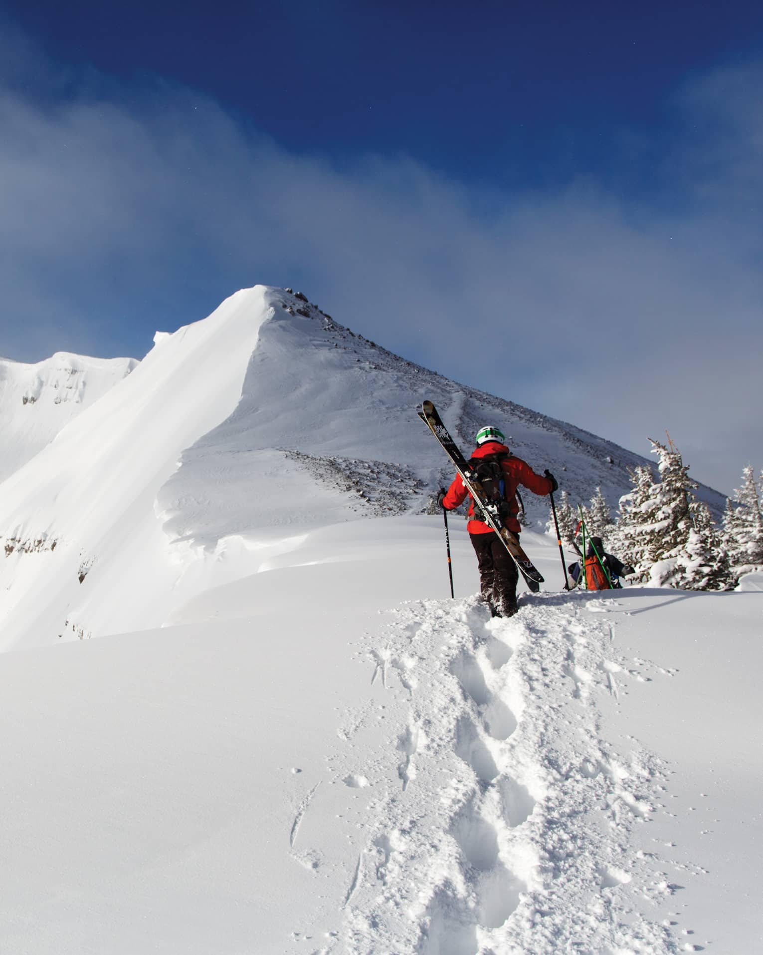 Two people with skis on their backs walking in snow.
